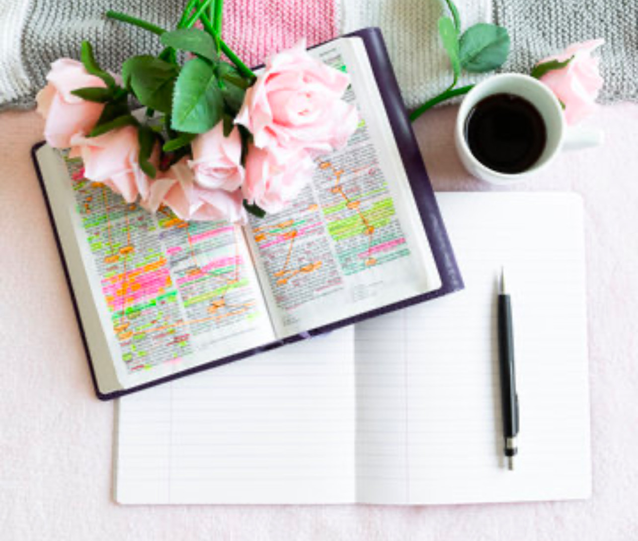 A notebook with a bible, a bouquet of flowers laying on the bible and a cup of coffee