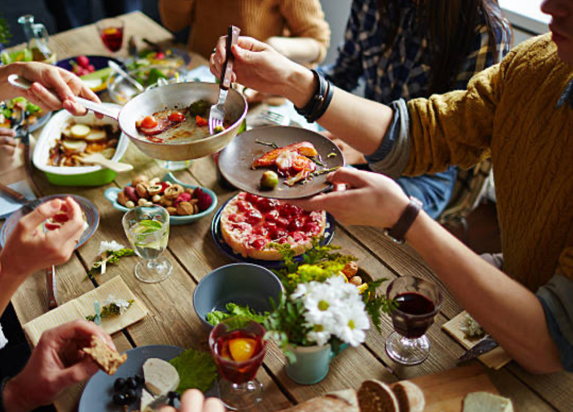 A long table with family style food set up and people sitting at the table eating and getting food